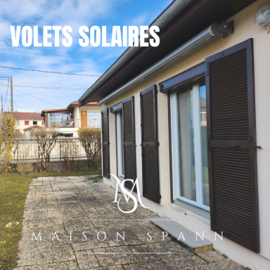 Nos volets solaires Volets solaires sur une façade de maison avec jardin et allée en pierre.