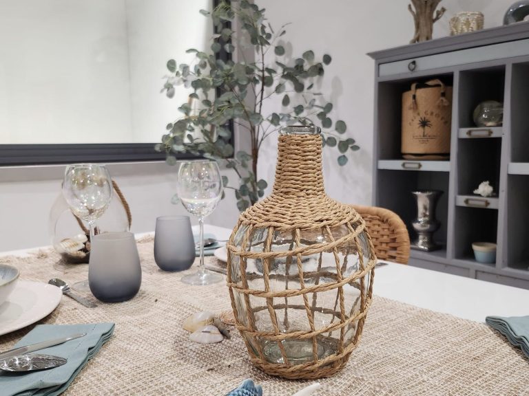 aménagement intérieur par Maison Spann Carafe en osier sur une table décorée, avec des verres et des éléments naturels en arrière-plan.